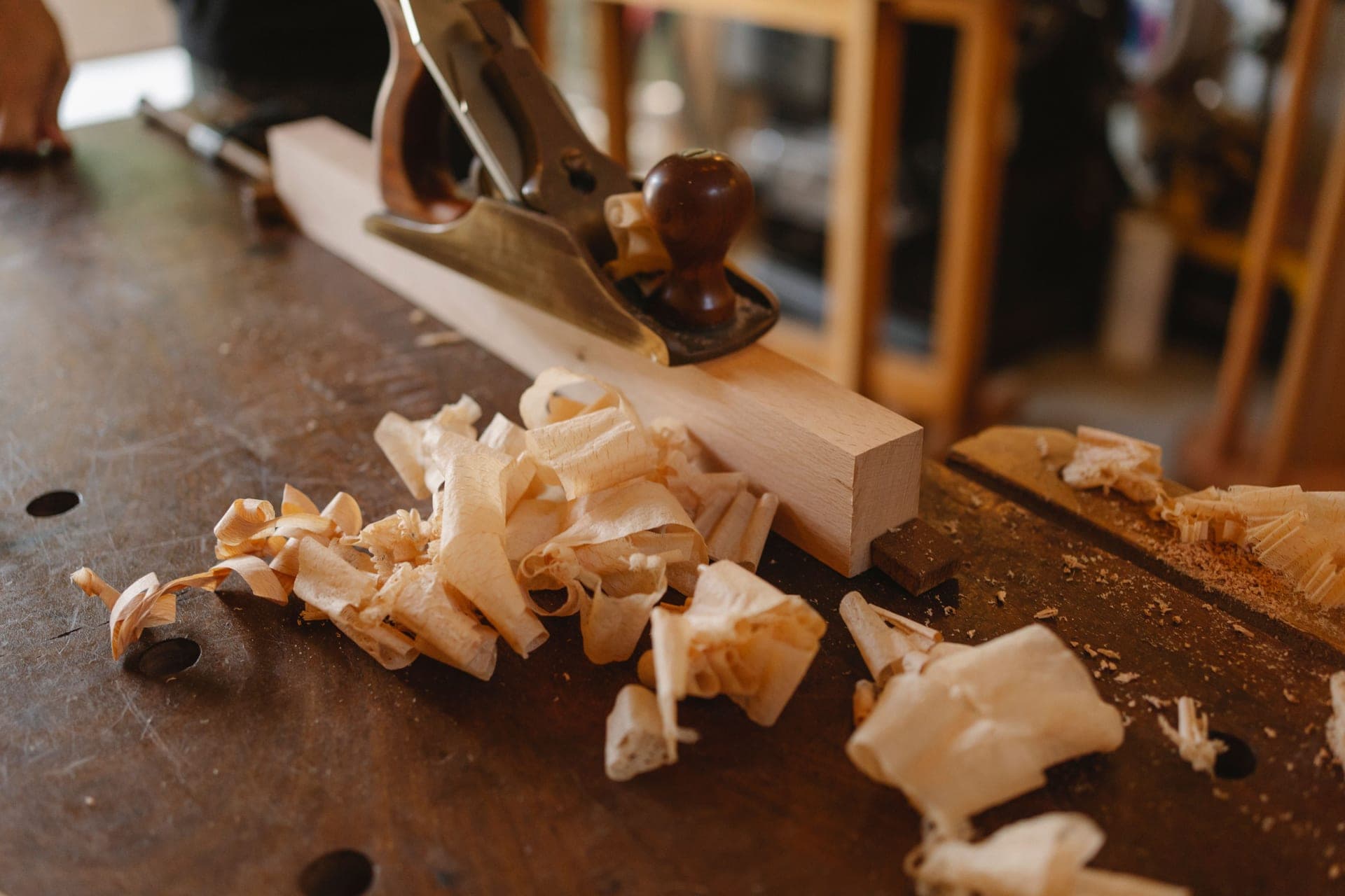 A hand plane and a curl of shavings resting on a wooden workbench